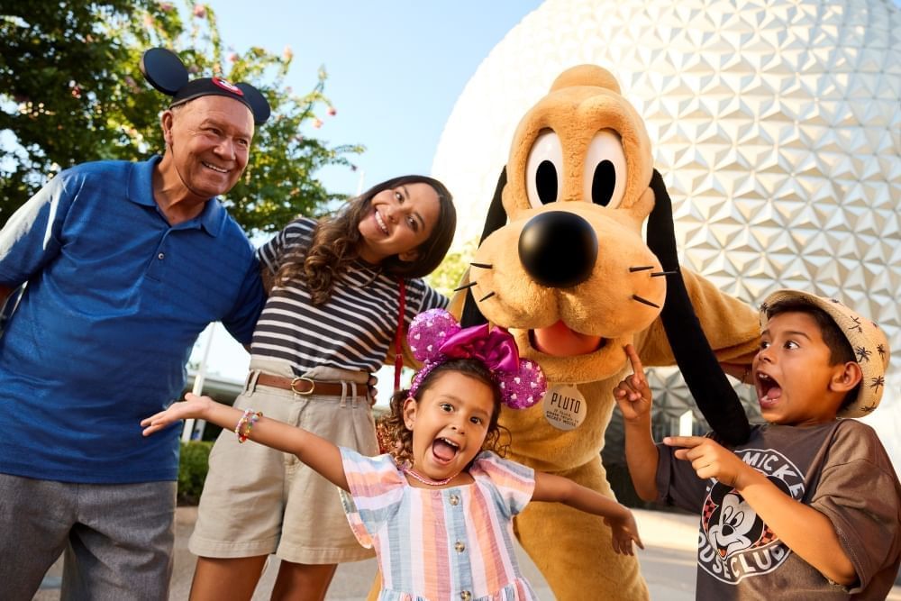 A mom, dad, and two children in Disney gear pose with Pluto in front of Spaceship Earth at EPCOT. 