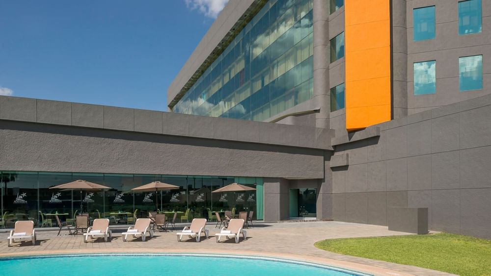 Sunny pool deck featuring lounge chairs, patio dining, and the modern hotel building at Real Inn Nuevo Laredo