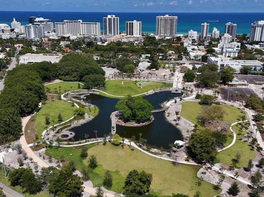 Aerial view of Bayshore Park with pond and trees, surrounded by cityscape and ocean horizon near Tradewinds Apartment Hotel