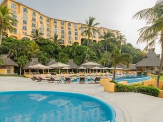 Multi-story hotel exterior featuring several outdoor pools and thatched palapas at Quinta Real Acapulco