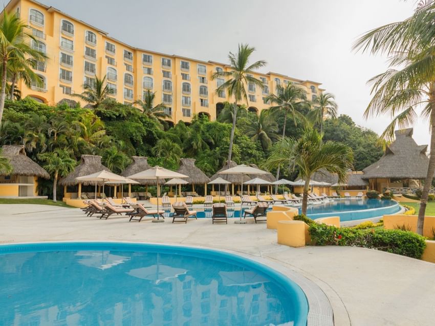 Multi-story hotel exterior featuring several outdoor pools and thatched palapas at Quinta Real Acapulco