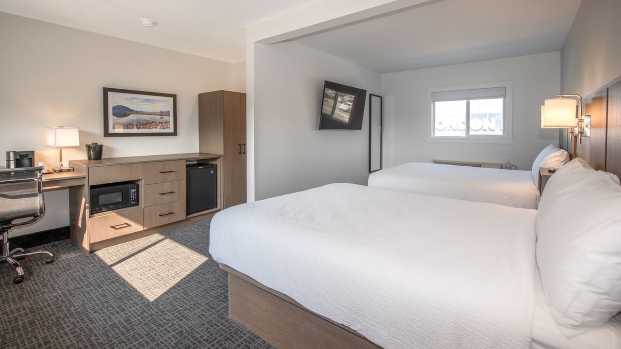 A hotel room with two beds, a desk, a chair, and a small kitchen area.