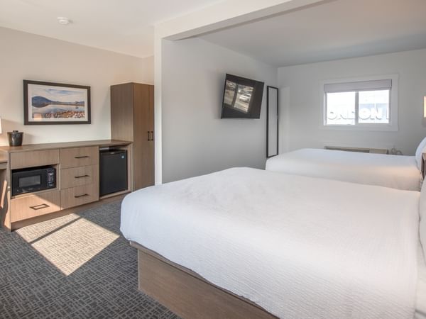 A hotel room with two beds, a desk, a chair, a TV, and a window.