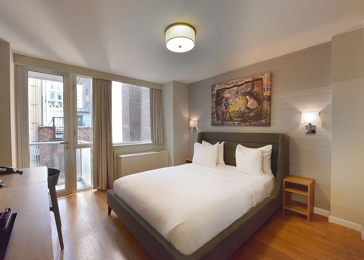 A hotel room with a large bed, desk, chair, and balcony
