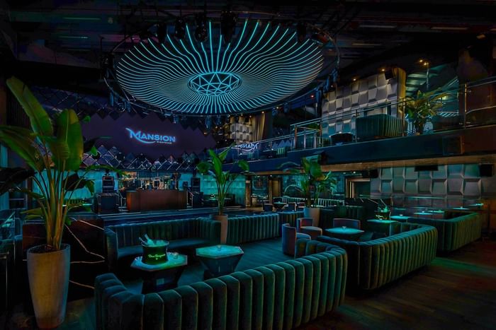 Mansion Nightclub at Paradox Vancouver with large circular blue light fixture, green couches, and tall potted plants.