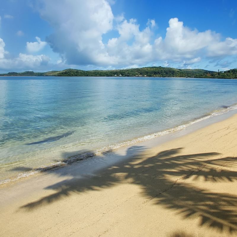 Serene sandy beach with gentle waves, and distant lush green hills, near Warwick Hotels and Resorts at Fiji