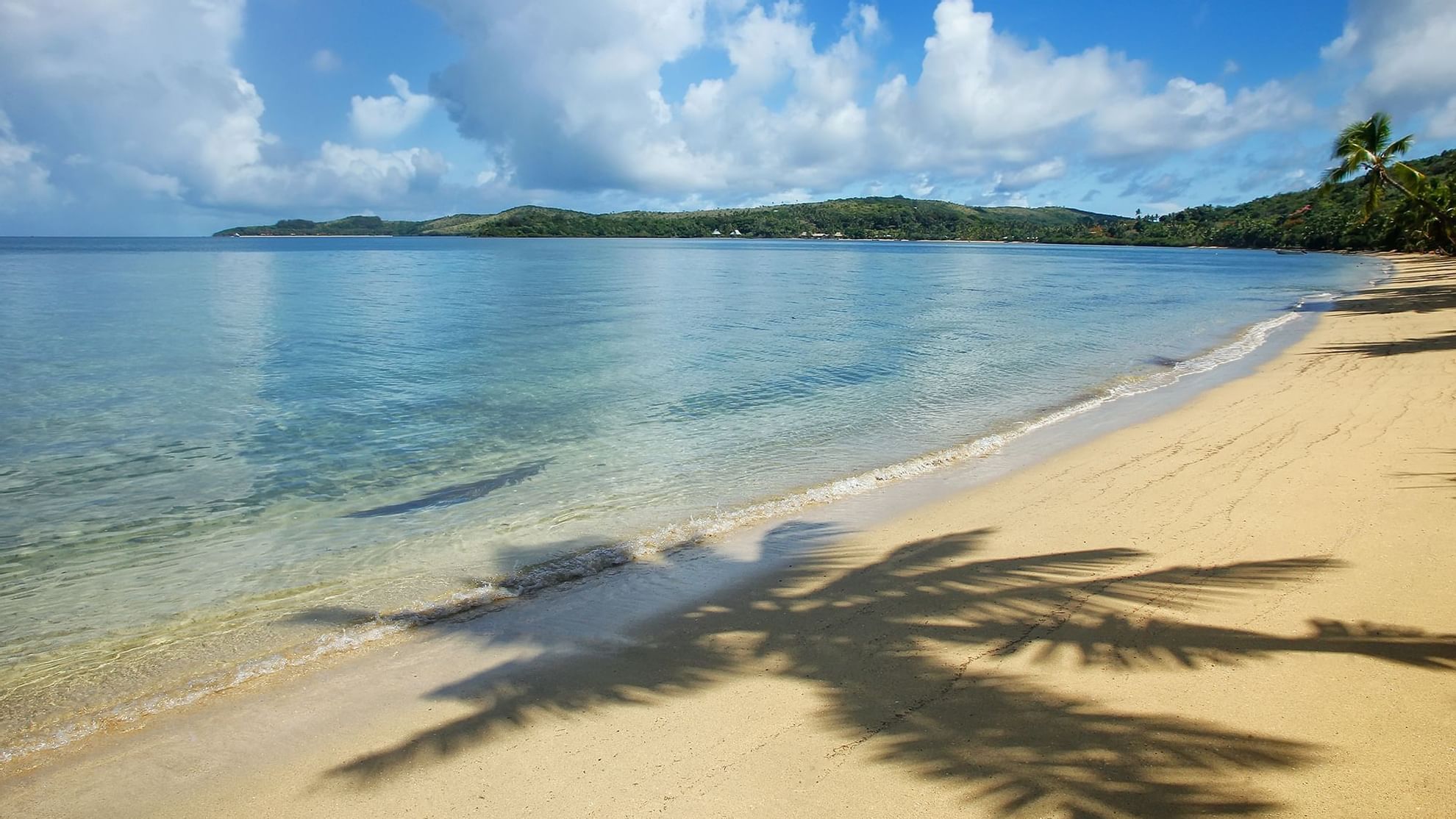 Serene sandy beach with gentle waves, and distant lush green hills, near Warwick Hotels and Resorts at Fiji