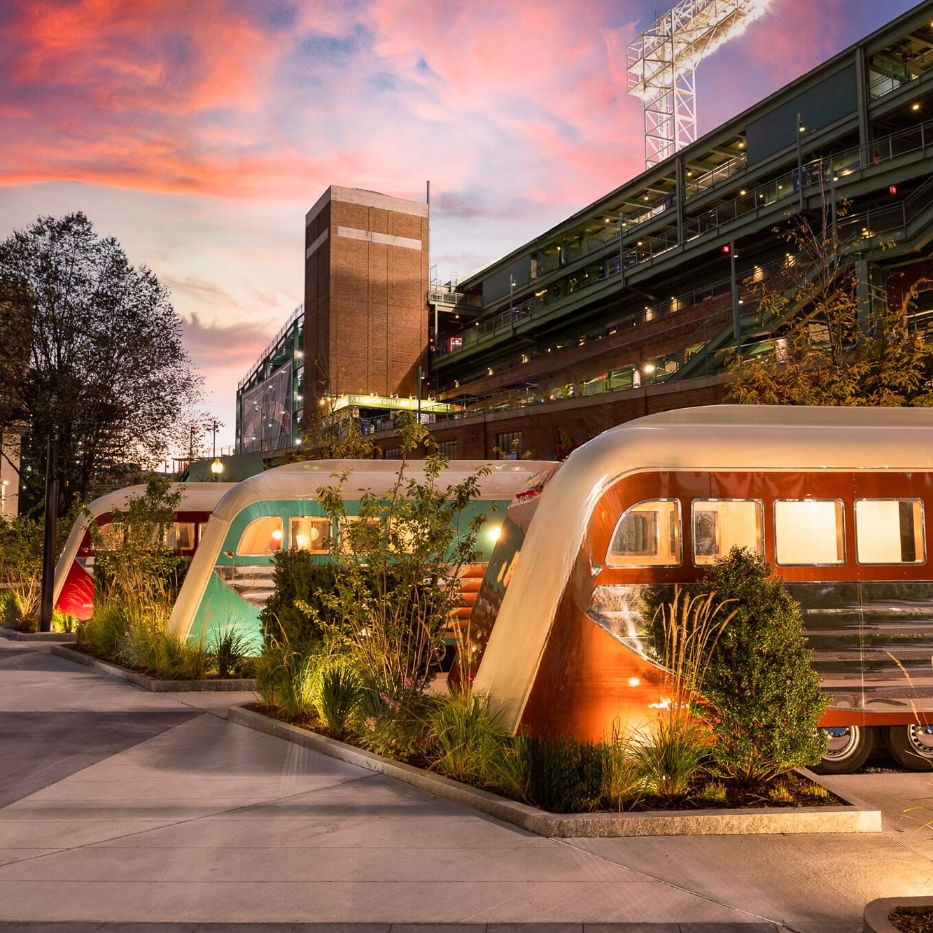 Vintage camper trailers converted into illuminated guest accommodations beneath a colorful sunset sky at a modern hotel property