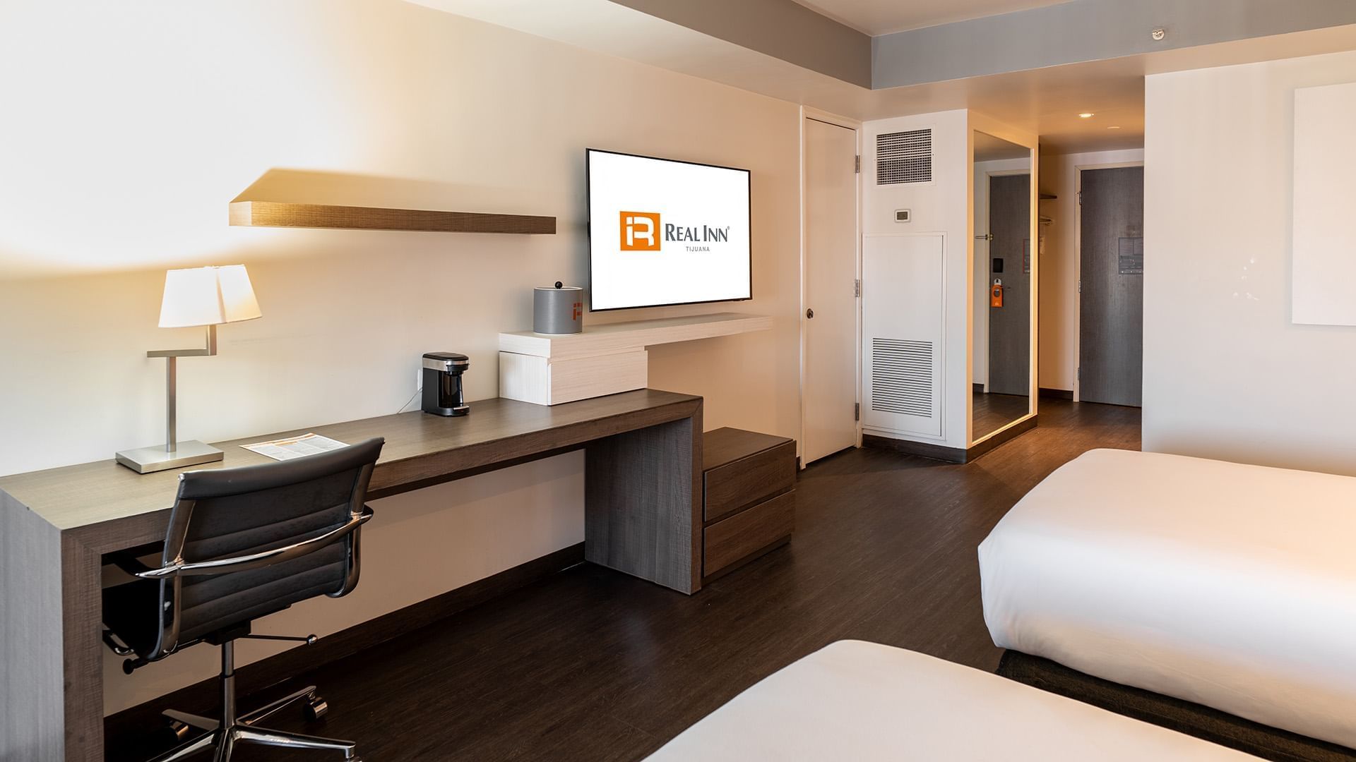 Wall-mounted TV and work desk facing the cozy bed in the Two Double Deluxe Room with wooden floors at Real Inn Tijuana