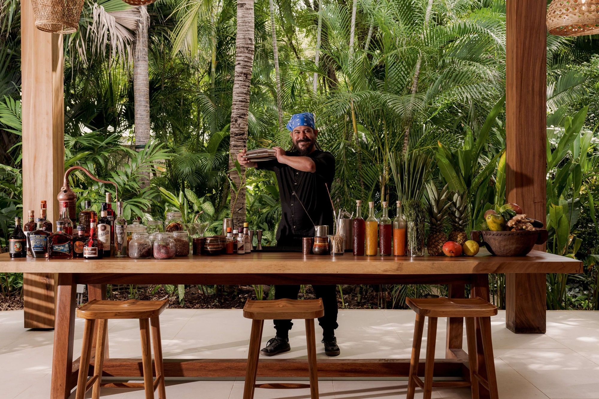 Expert mixologist preparing craft cocktails at a wooden bar surrounded by palms at Cala Luna Boutique Hotel