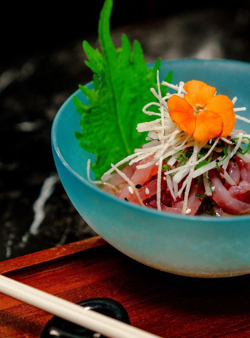 A bowl of sashimi topped with shredded vegetables on a wooden tray at The Kitchens