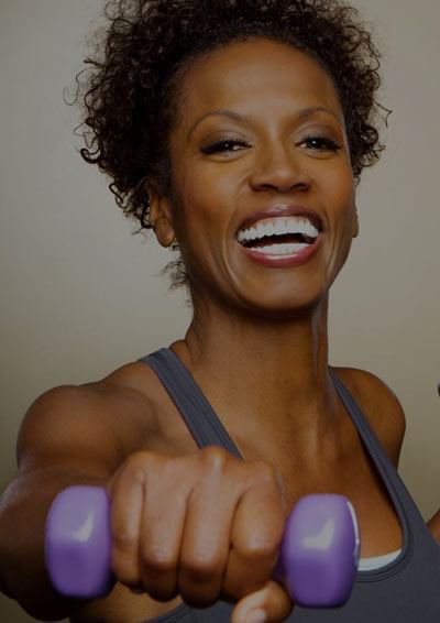 Woman in a tank top showing bicep muscles while holding purple dumbbells at Azalai Hotel Ouagadougou