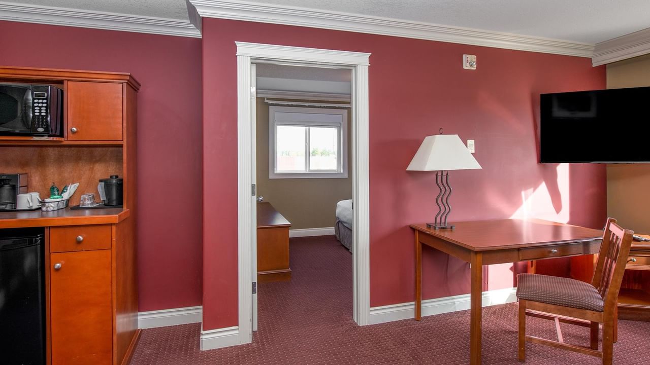 Suite with red walls, kitchenette, wooden desk, and view into bedroom at Coast Edson Hotel