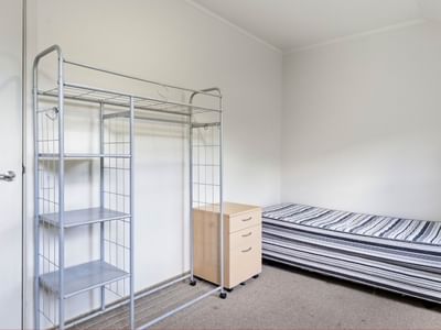 A tidy room with a metal shelving unit, a small dresser, and a bed at UniLodge Stafford House.