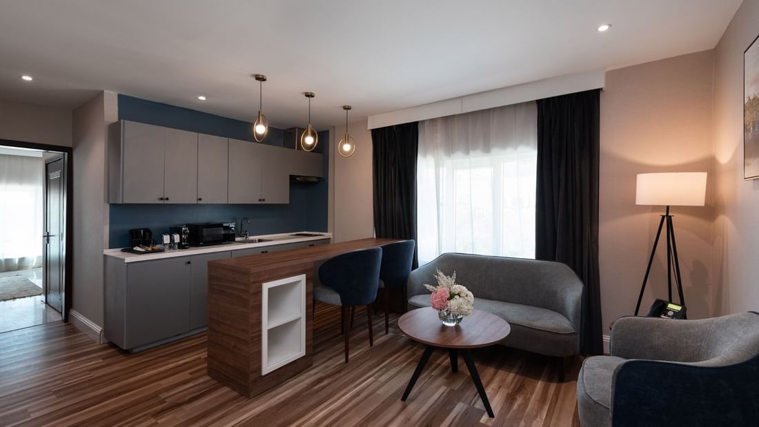 Wooden breakfast bar by a grey sofa and kitchenette with hanging globe lights in Junior Suite City View at Warwick Al Jubail