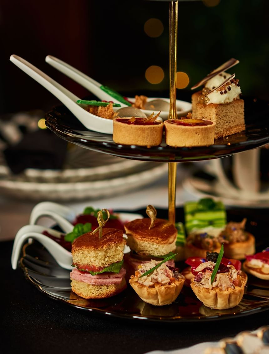 Two-tiered tray with assorted finger foods, including tarts, sandwiches, and canapes, served at the Hotel Arista.