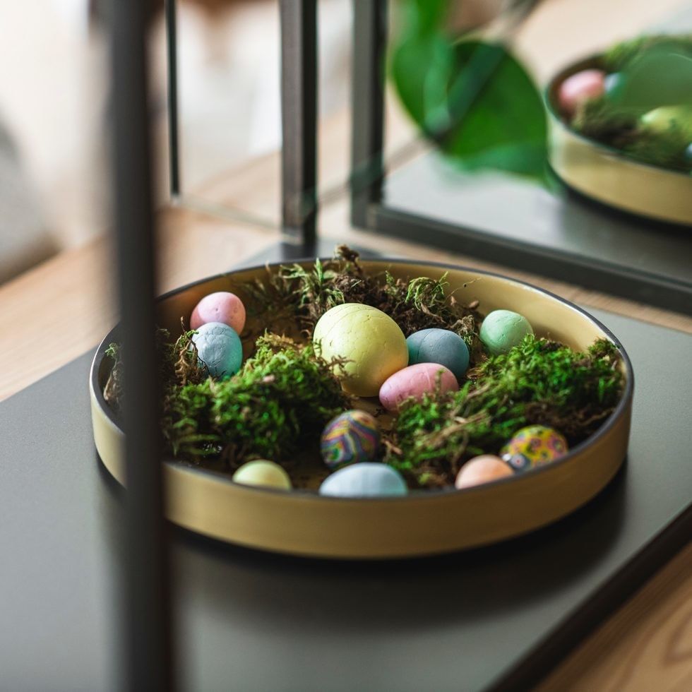 Ostern mit bunten Eiern und Moos in einer goldenen Schale auf einem Tisch.