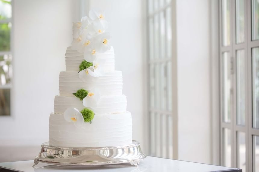 White wedding cake adorned with elegant orchids and green accents, displayed on a silver platter at Park Hyatt Saigon