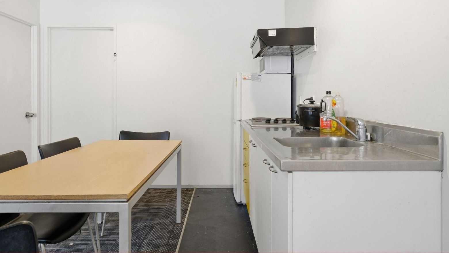 Simple kitchen with a dining table and modern white cabinets at Student Living Auckland Anzac.