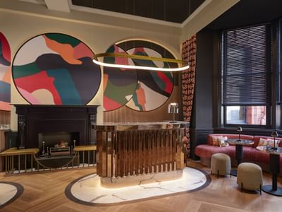 Colourful lobby Reception at The Met Hotel Leeds, England, with a copper desk, velvet sofa, and abstract circular artwork