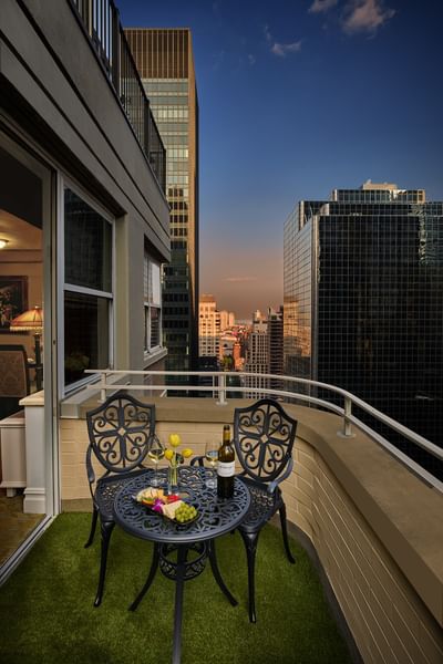 Private balcony with two metal chairs and a table set with wine & snacks between skyscrapers at The Kimberly Hotel