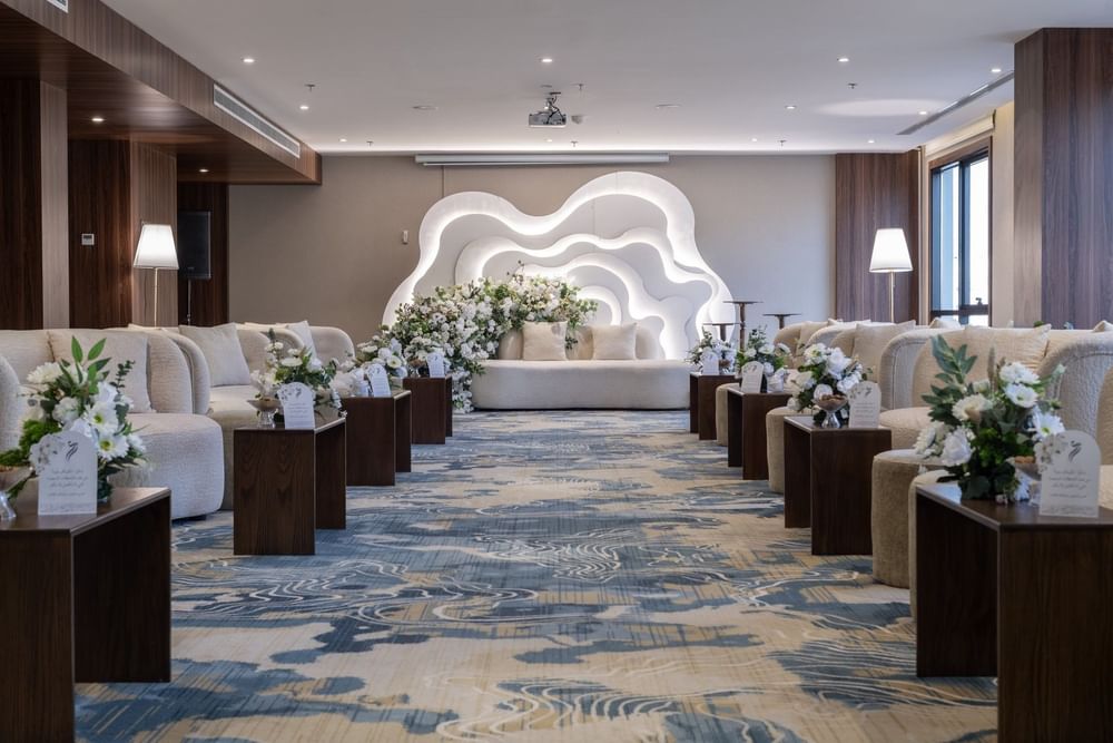 Cream sofas surrounding flower arrangements on a blue rug under bright lights in Amarige Hall at Warwick Hotels and Resorts