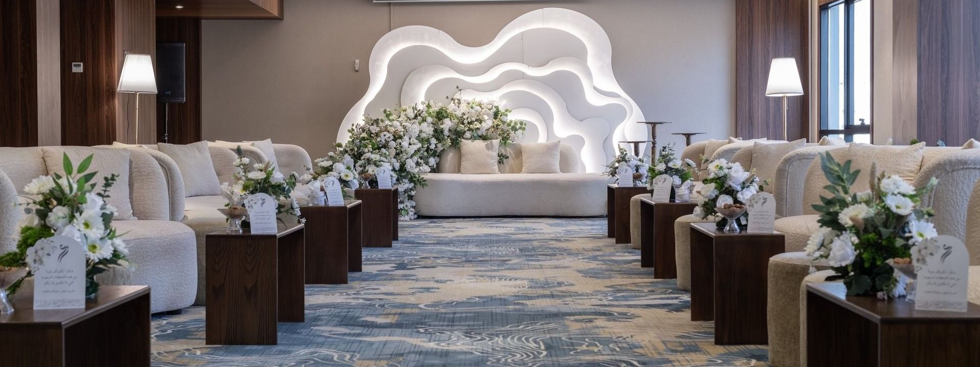 Cream sofas surrounding flower arrangements on a blue rug under bright lights in Amarige Hall at Warwick Hotels and Resorts