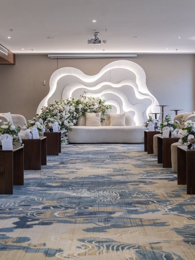 Cream sofas surrounding flower arrangements on a blue rug under bright lights in Amarige Hall at Warwick Hotels and Resorts