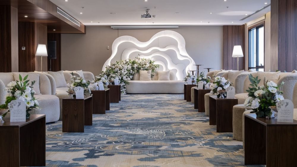 Cream sofas surrounding flower arrangements on a blue rug under bright lights in Amarige Hall at Warwick Hotels and Resorts