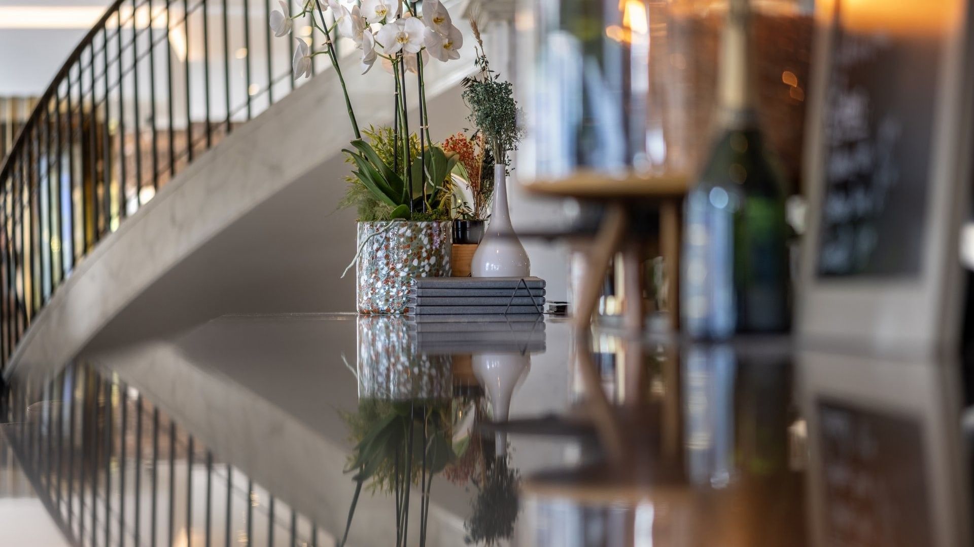 Vase avec des fleurs posé sur une surface réfléchissante près d'un escalier au Téséo Bar à Warwick, Genève.