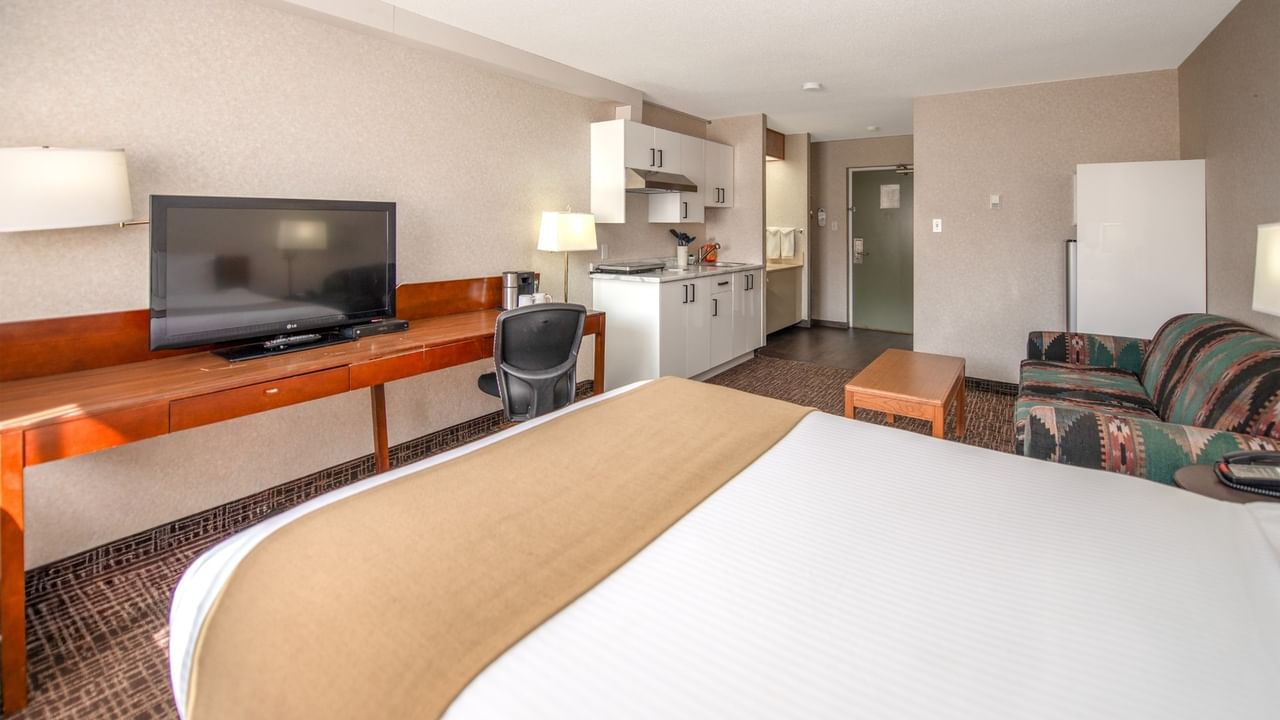 Hotel room with bed, desk, TV, chair, couch, kitchenette, and refrigerator.