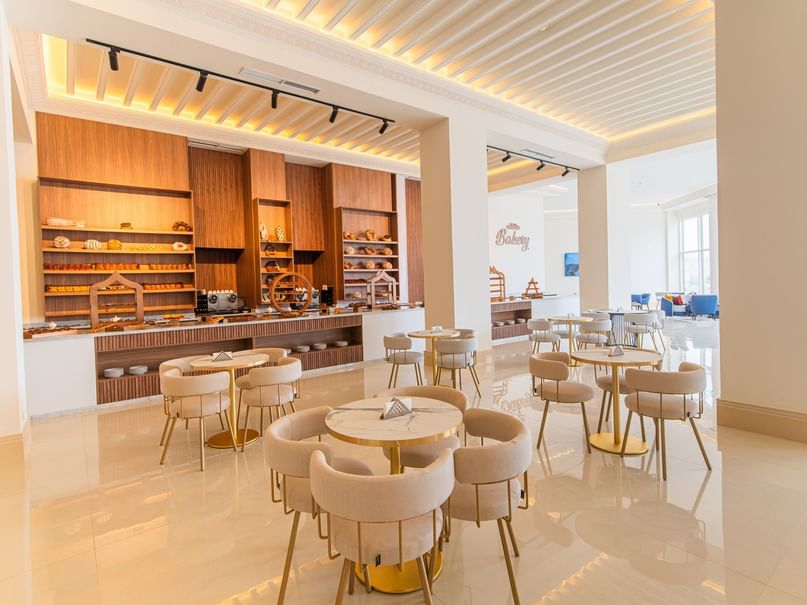 Modern cafe interior with tables, chairs, and a counter with food displays.