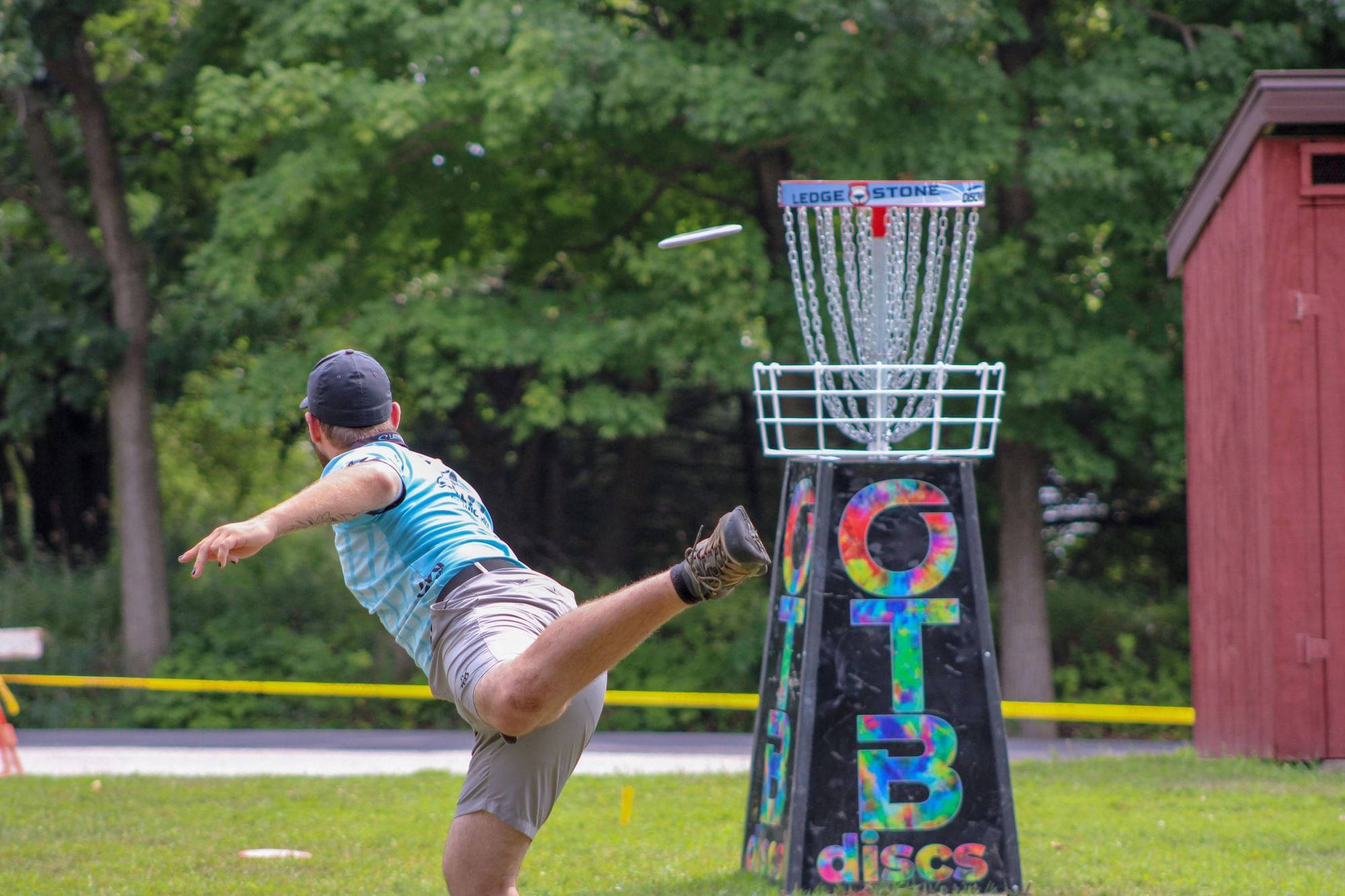 Man throwing frisbee into disc golf goal.