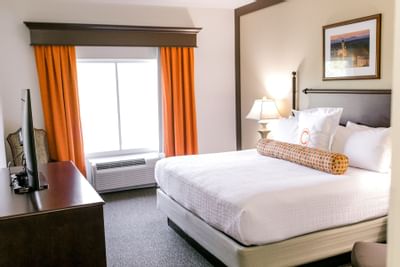 king bed with white sheets next to window and orange curtains