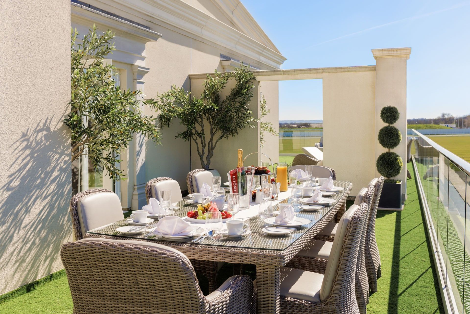 Woven dining chairs & table with breakfast setup on a sunny artificial grass terrace in The Empress Suite at Polo Club Hotel