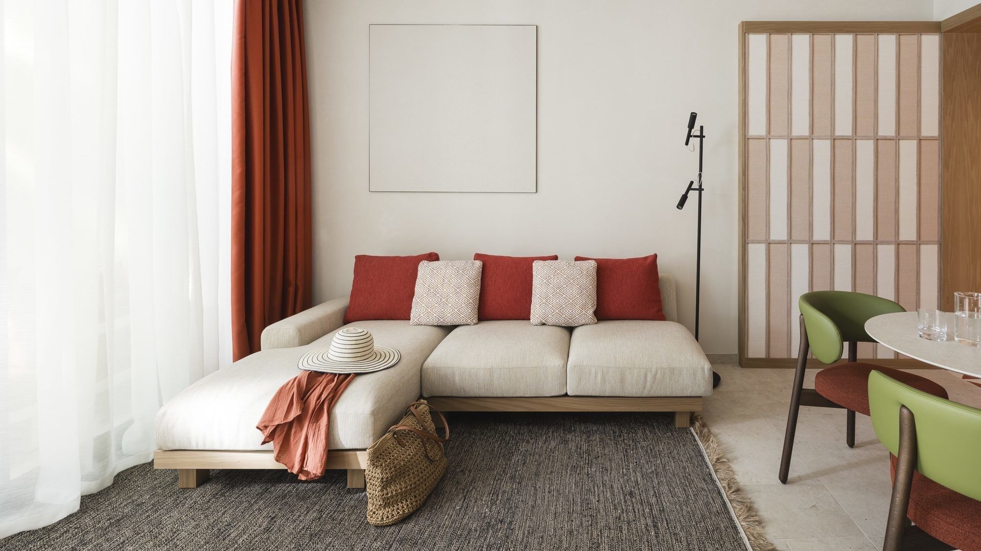 Divano bianco con cuscini rossi e bianchi, tavolo rotondo, sedie verdi e arazzo in una stanza moderna.