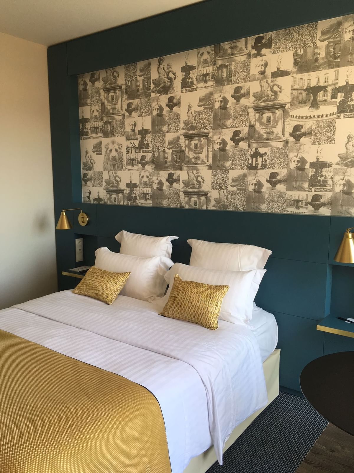 Chambre à coucher avec lit double, tête de lit murale décorée, et deux lampes murales dorées.