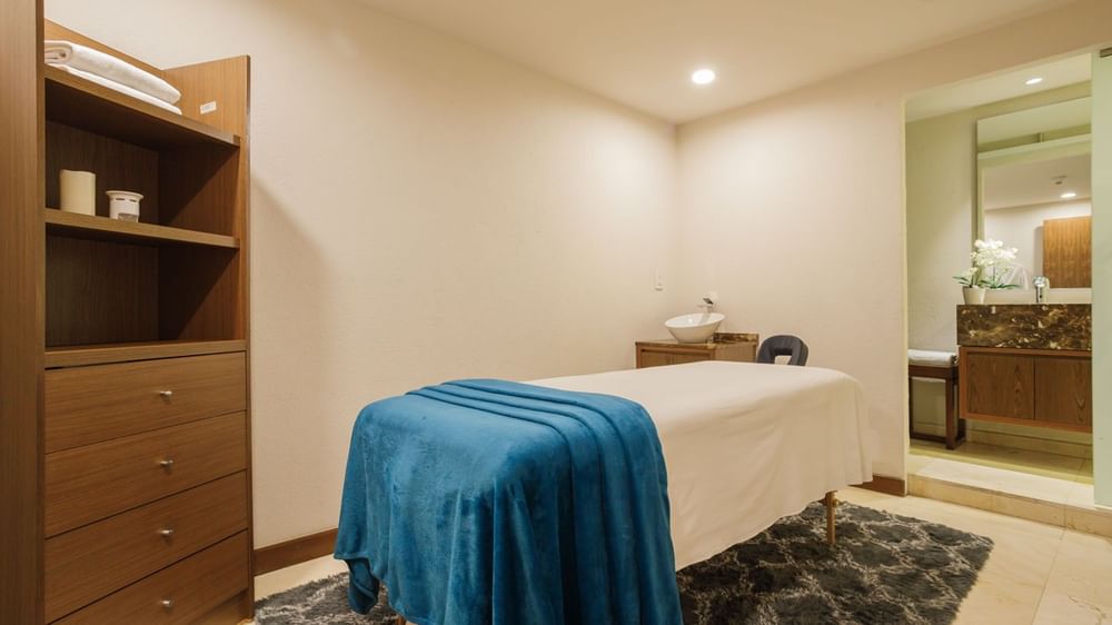 Serene massage room at Camino Real Pedregal Mexico, featuring a blue blanket on the table and a wooden cabinet