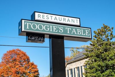 Restaurant sign for Toogies Table with autumn foliage and historic building at Bardstown Motor Lodge
