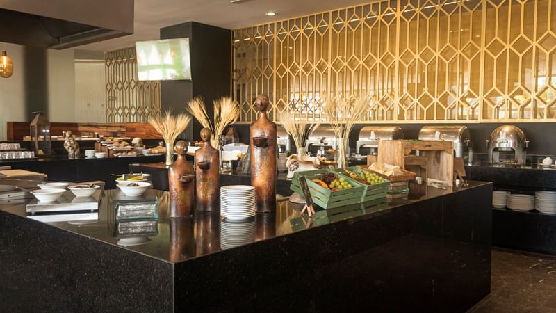 Área de buffet en restaurante La Huerta con estatuas decorativas y bandejas de comida en Camino Real Puebla Angelopolis