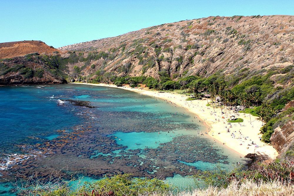 A wide-angle view of a beach with clear blue water and a mountainous backdrop.