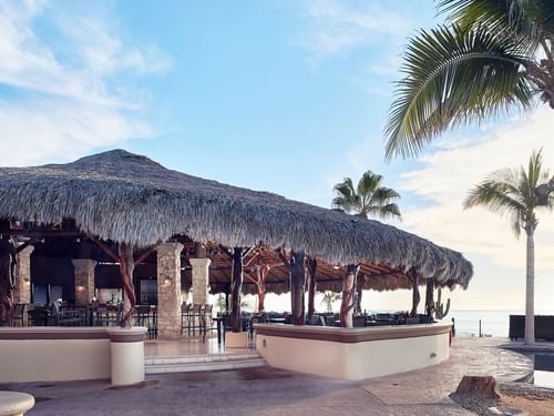 Sirenas Restaurant's exterior with a thatched roof, bar stools, and ocean views at Hacienda del Mar Los Cabos.