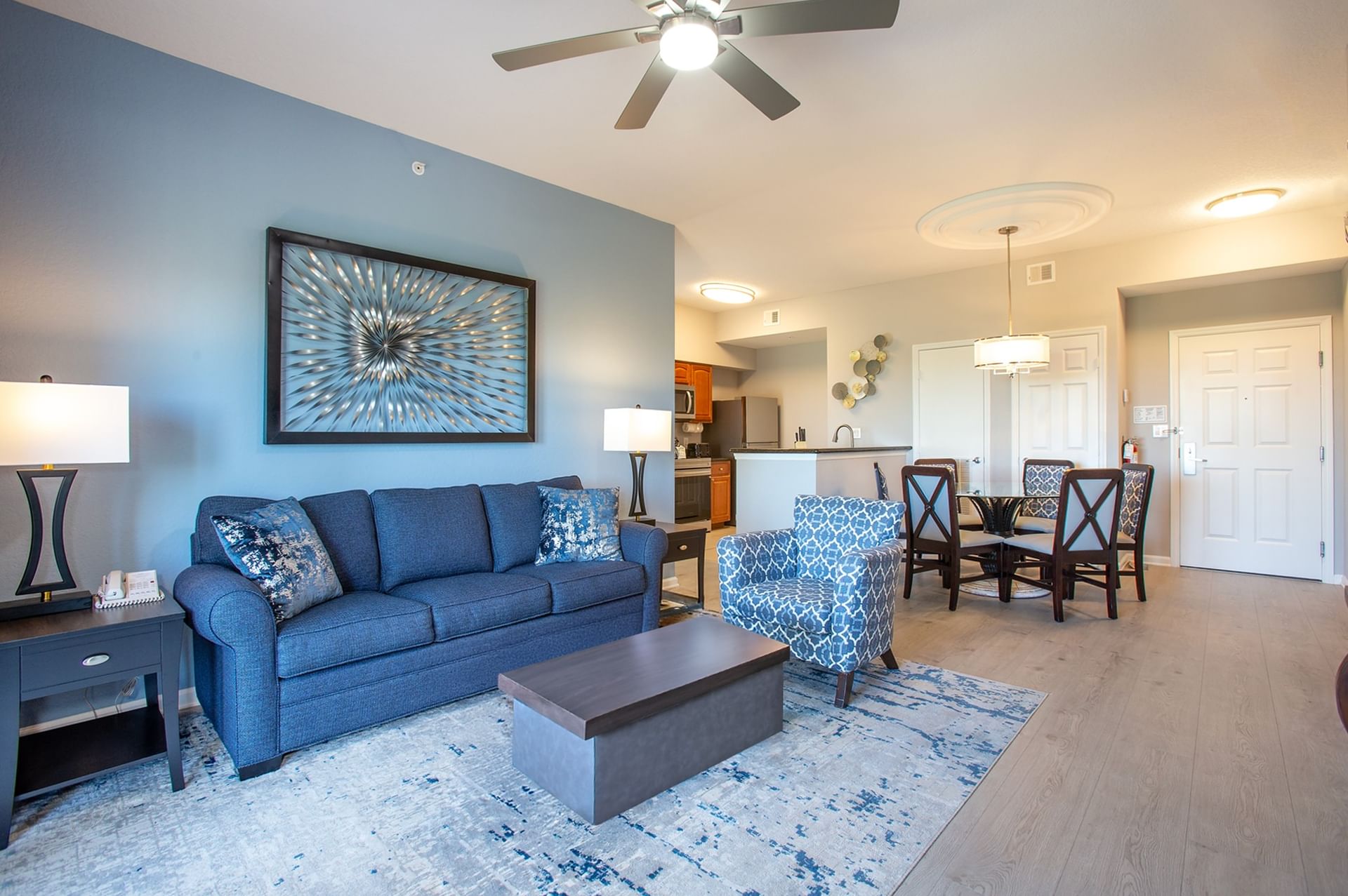 A wide view of a living room and dining area with a kitchenette in the background.