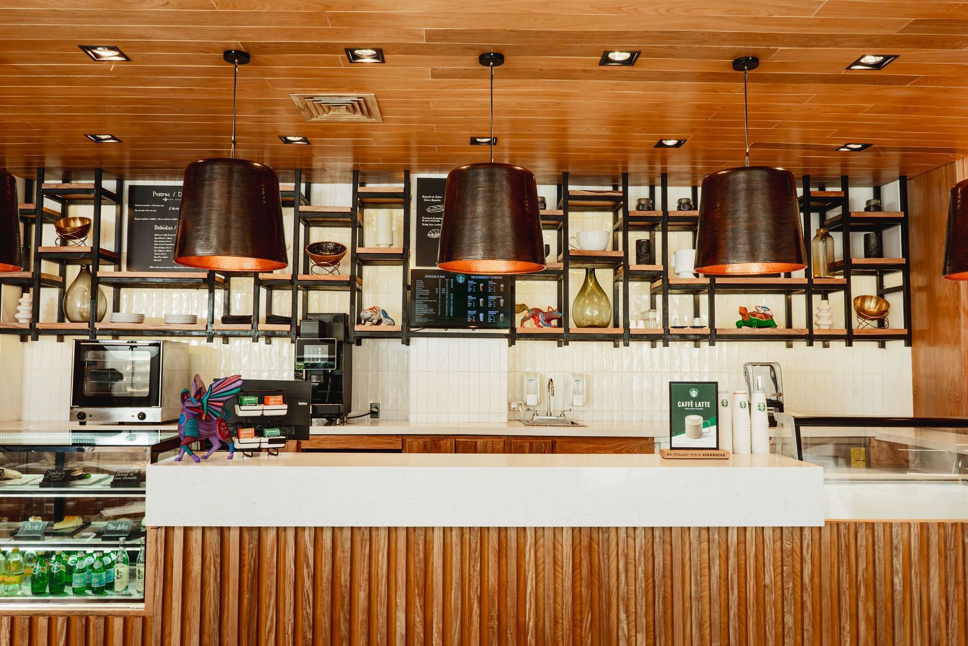 Warmly lit cafe counter with three large pendant lights overhead in Library Café & Deli at Camino Real Zaashila Huatulco