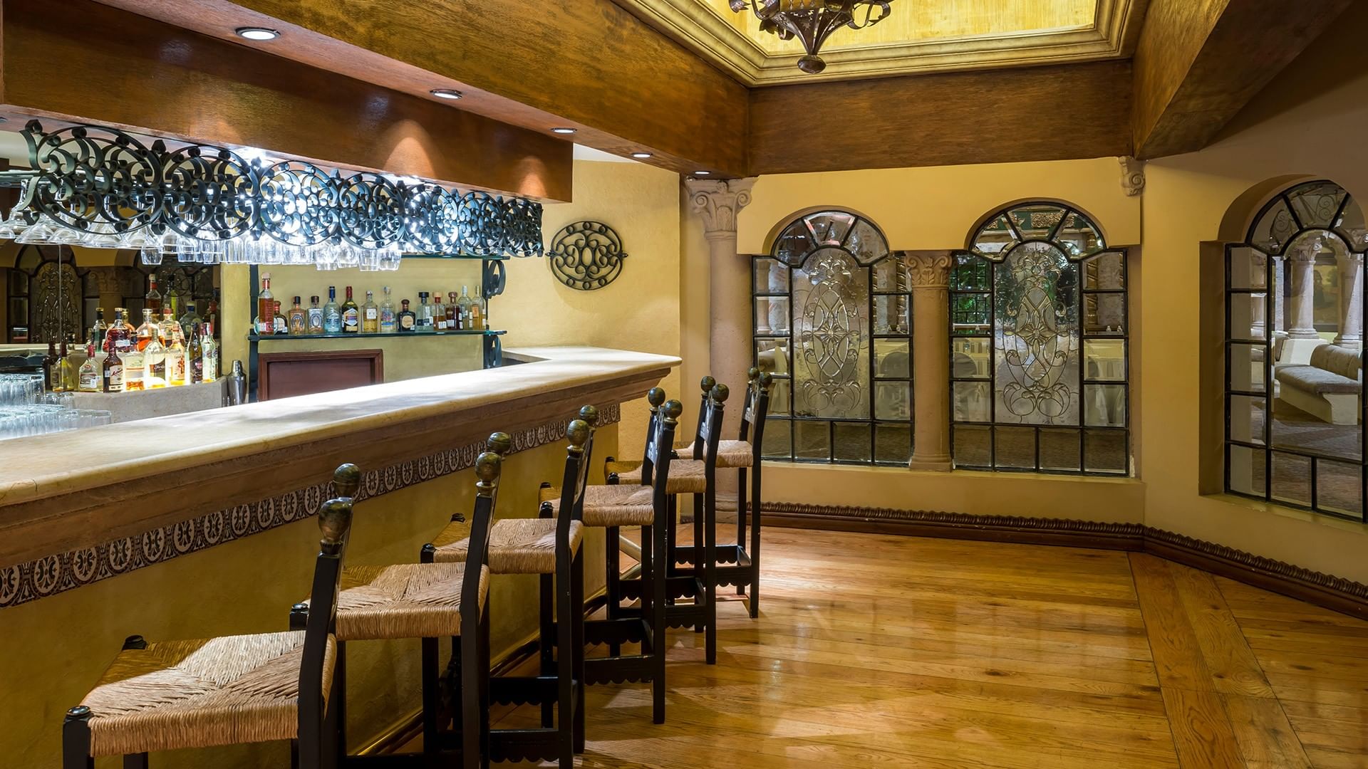 Restaurant bar with decorative ironwork, arched windows, and wooden beam ceiling at Quinta Real Aguascalientes