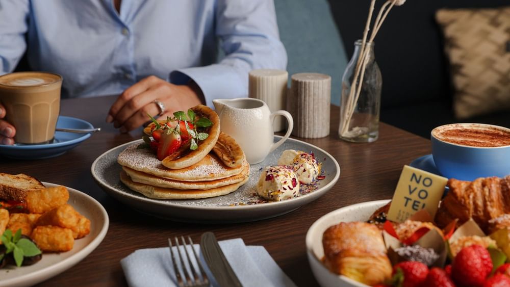 Breakfast table with pancakes, pastries, fresh fruit, and coffee