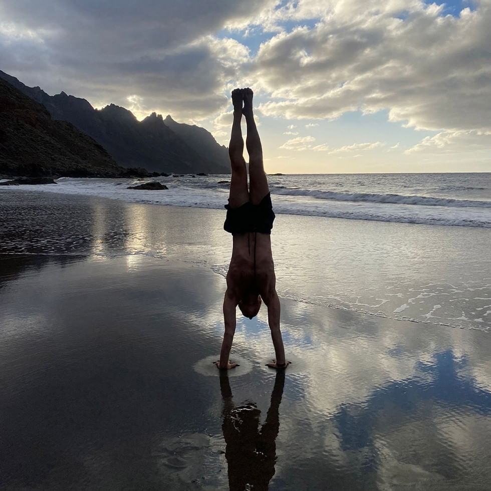 Man performing a handstand on the beach at sunset for Spring Flow & Awakening event.