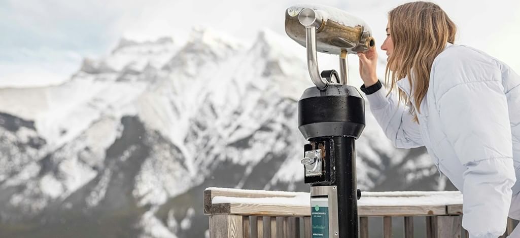 A person looks through a public telescope at a park near Banff.