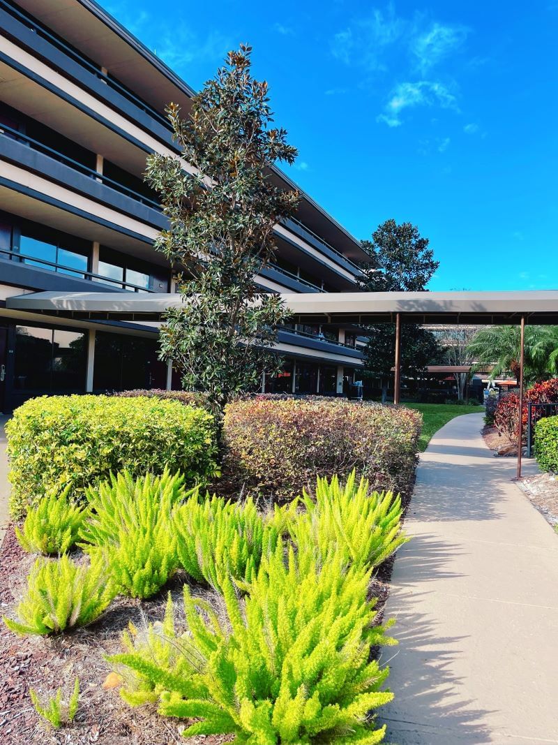 The side exterior of Rosen Inn at Pointe Orlando, featuring a veranda and vibrant, green vegetation.