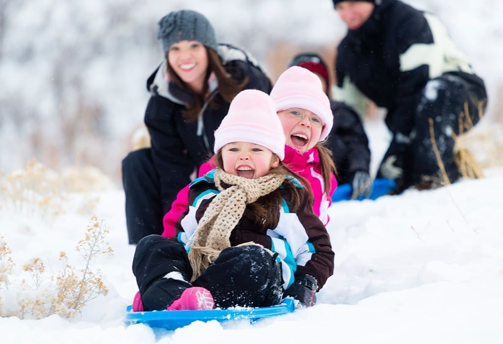 kids sledding on snow with mom